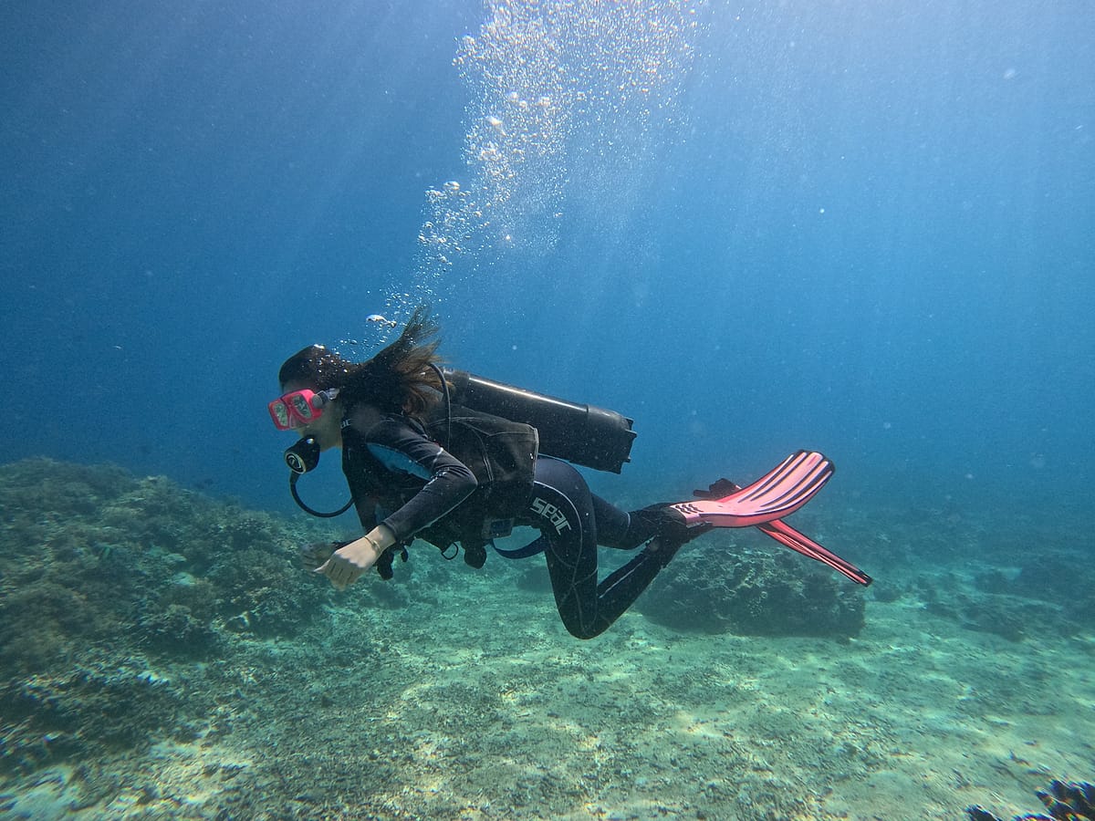 Penyelam berenang di atas terumbu karang dengan gelembung udara dan cahaya matahari di Kepulauan Gili